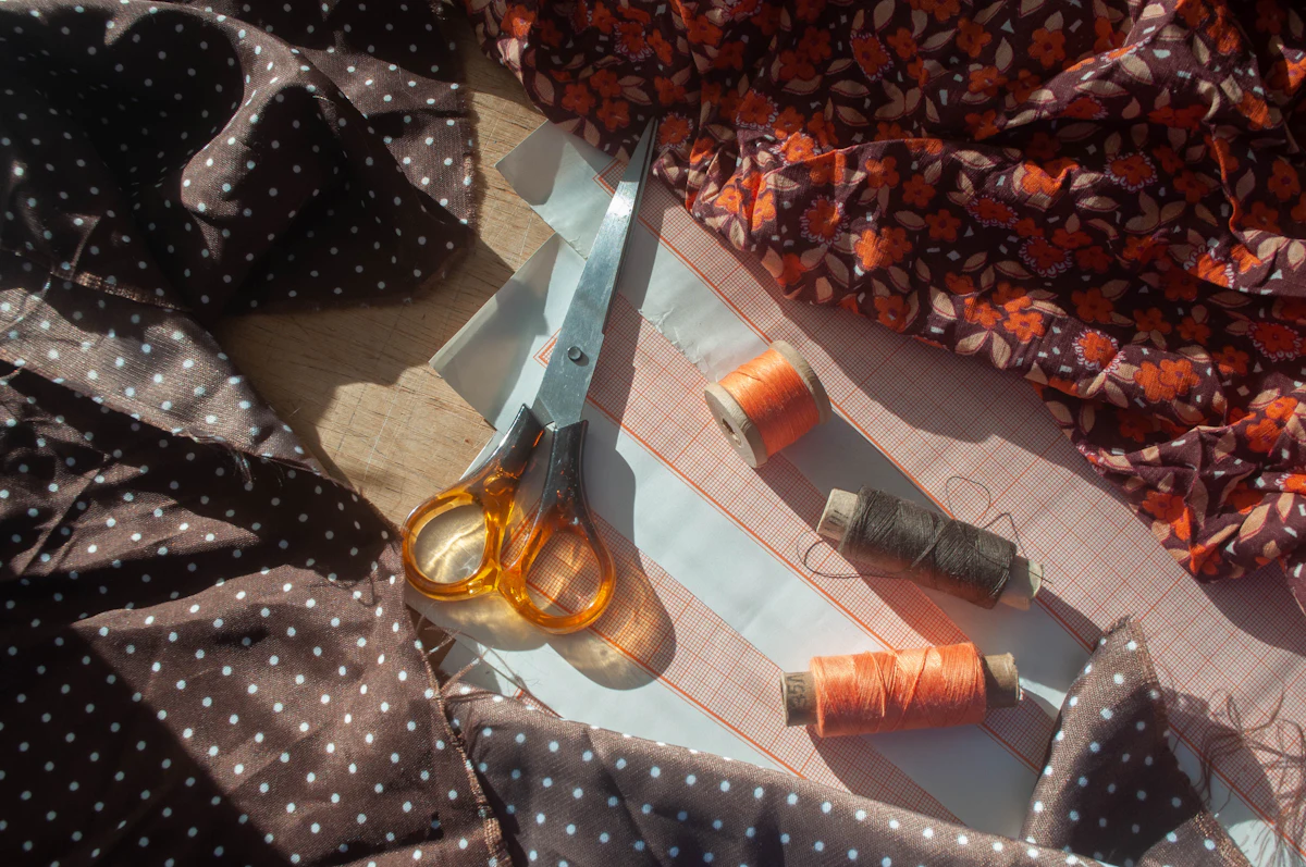 Scissors, orange thread and floral fabric on a sewing table